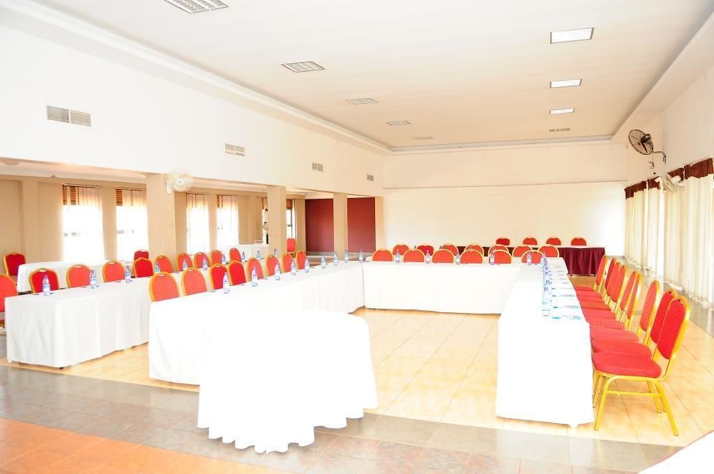 Una sala conferenze con lunghe tavole e sedie rosse, tovaglie bianche e pavimento piastrellato.