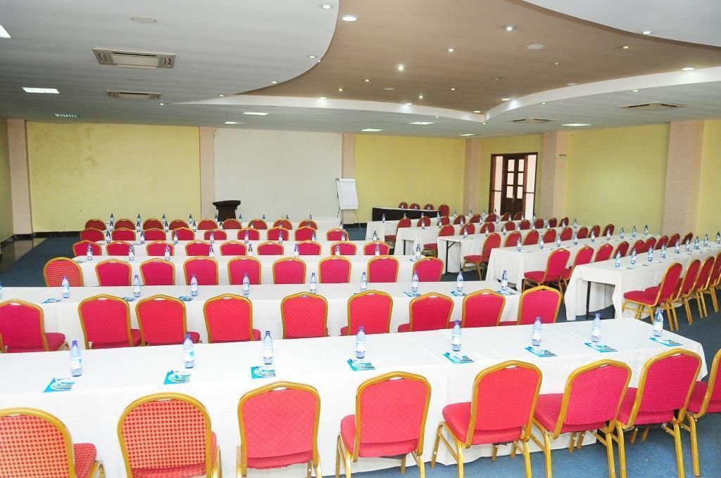 Une salle de conférence avec des rangées de chaises rouges et des tables blanches, équipée de bouteilles d’eau et de porte-noms.