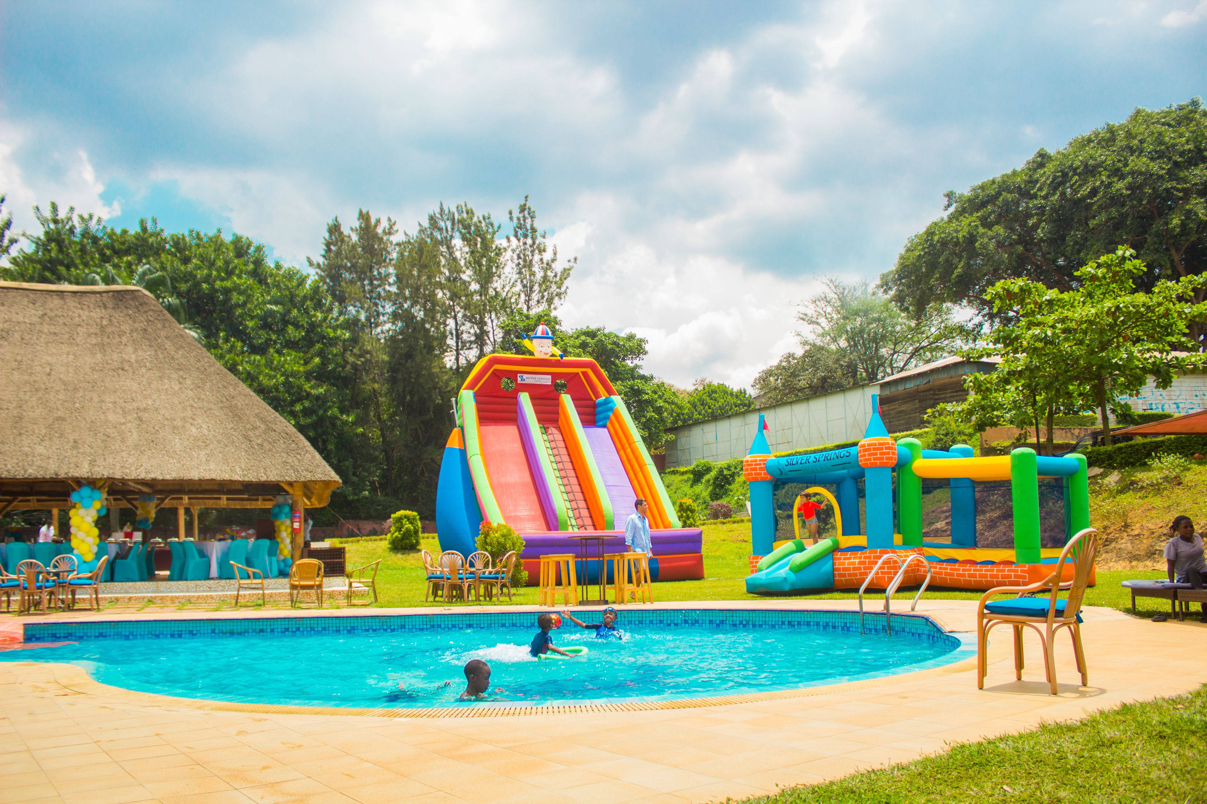 A swimming pool with inflatable slides and a thatched-roof structure.
