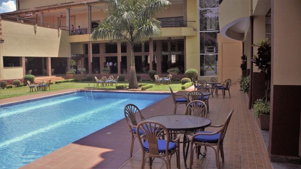A pool area with lounge chairs and tables, a palm tree, and a building with multiple floors and balconies.
