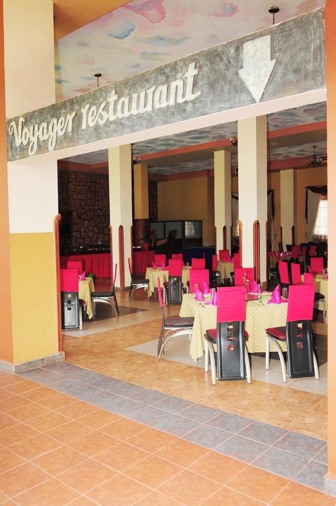 A restaurant with a sign reading 'Voyager Restaurant' and multiple tables with red chairs.