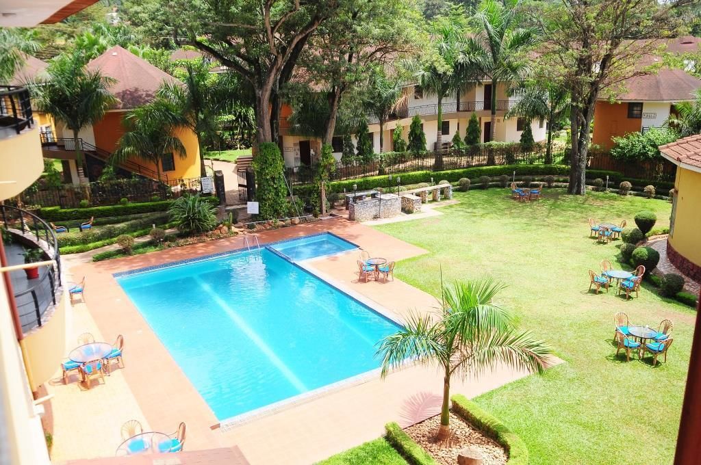 Piscina con sillas de descanso y mesas, rodeada de césped cuidado y árboles.