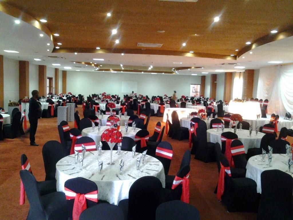 Un salón de banquetes con mesas redondas, sillas negras y cintas rojas y blancas.