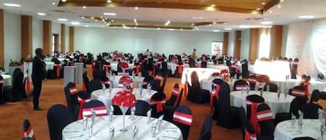 Un salón de banquetes con mesas redondas, sillas negras y cintas rojas y blancas.
