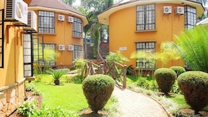 A yellow building with multiple air conditioning units, a paved pathway, and well-maintained greenery. - Silver Springs Hotel Uganda (Kampala)