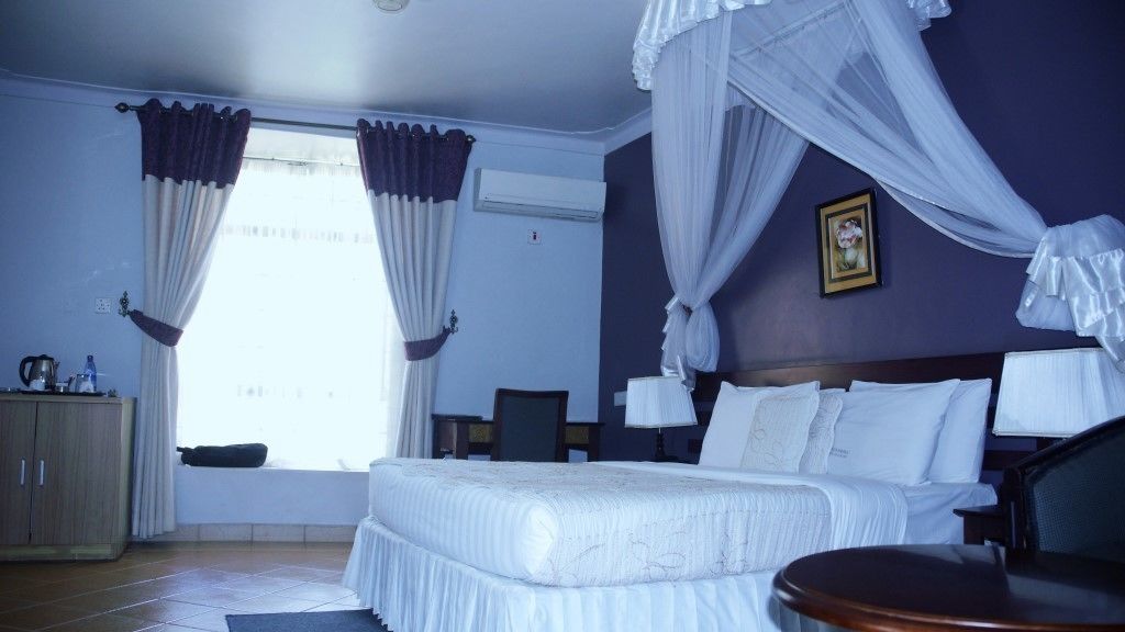 A hotel room with a bed, a bedside table, a chair, a window with curtains, and a picture on the wall.