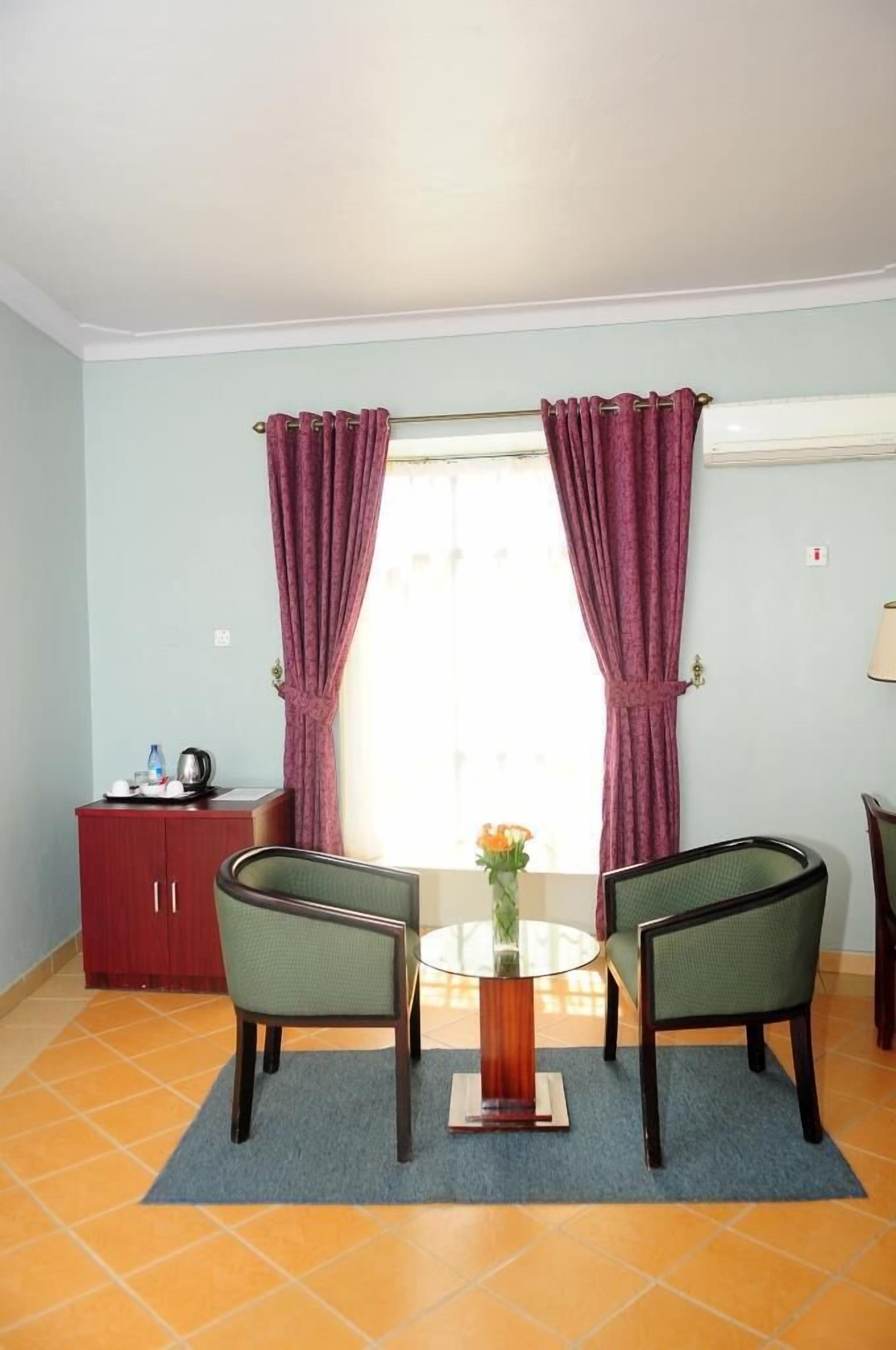 A room with a dining table, two chairs, a cabinet, and a window with curtains.