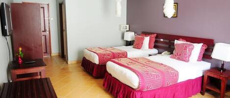 A hotel room with two beds, a wooden wardrobe, a small table, and a bedside table with a lamp.