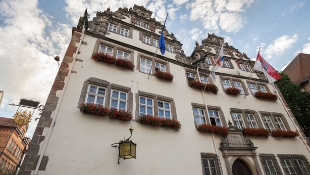 Un edificio histórico con múltiples ventanas, algunas con balcones de flores, y un farol tradicional.