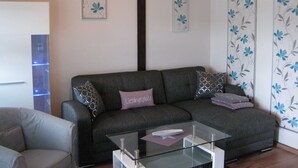 Una sala de estar con un sofá gris, una mesa de centro de vidrio y papel tapiz floral.
