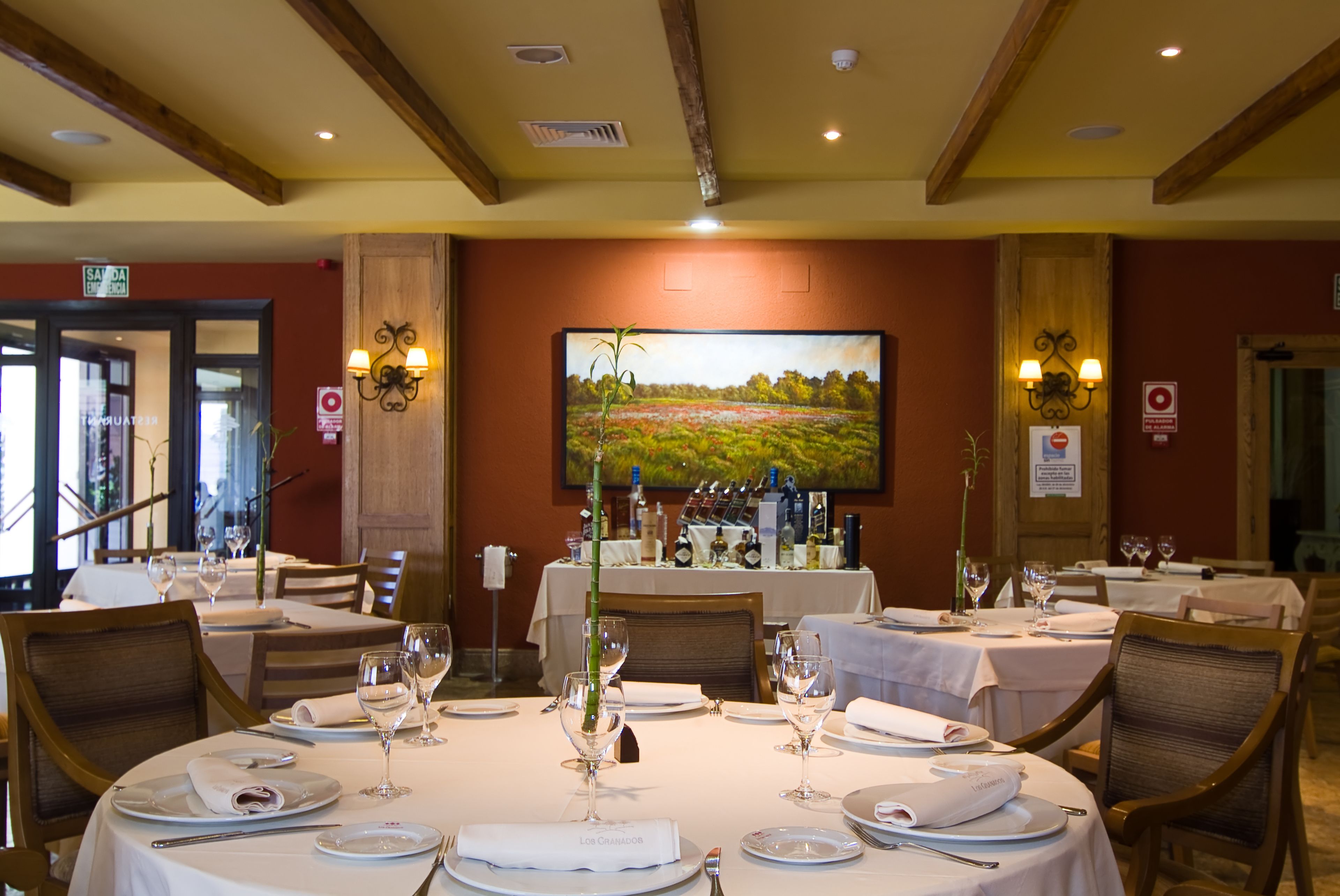 Comedor con mesas redondas dispuestas para el servicio, con manteles blancos y platos, vasos y cubiertos ordenados.