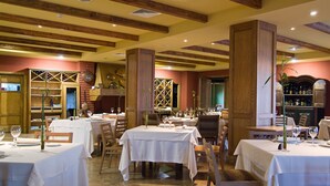 Un restaurante con varias mesas, vigas de madera en el techo y copas de vino en cada mesa.