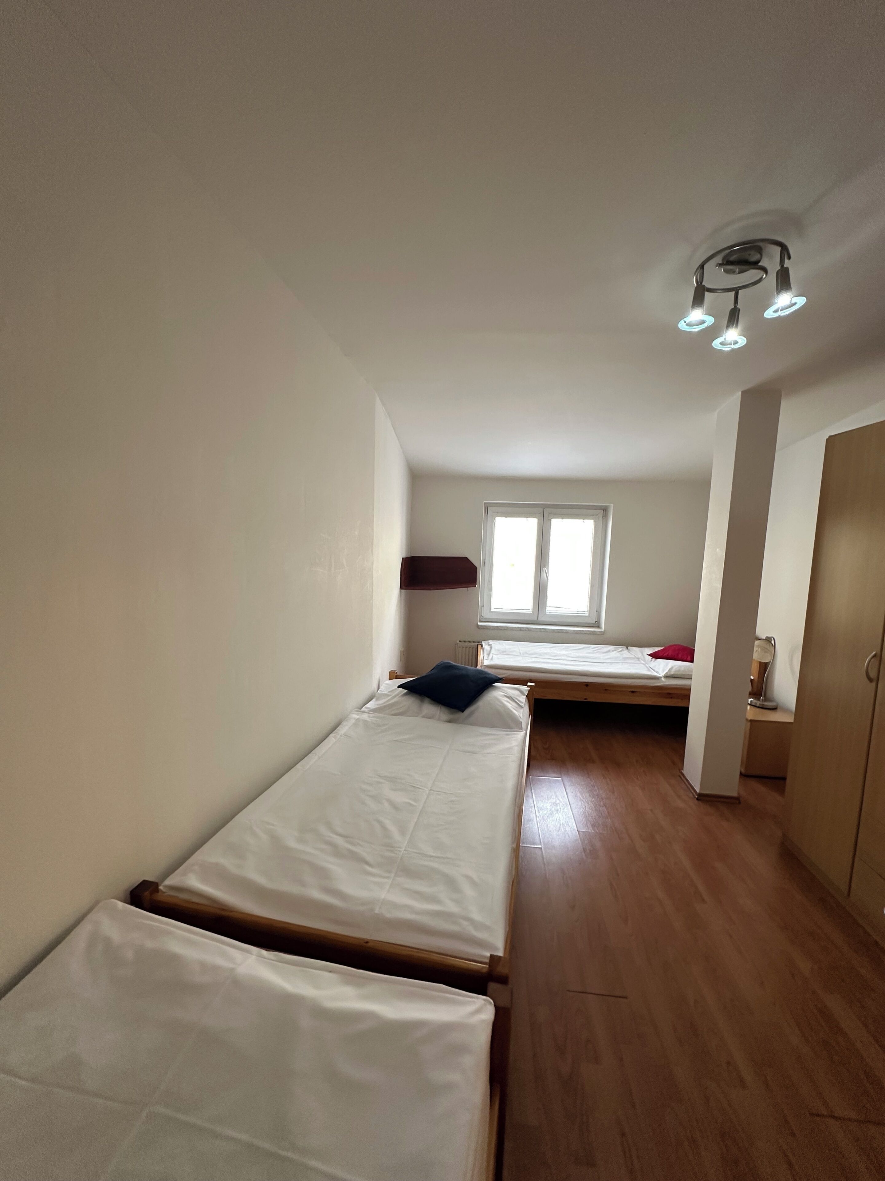 A room with two single beds, a window, a door, and a ceiling light fixture.