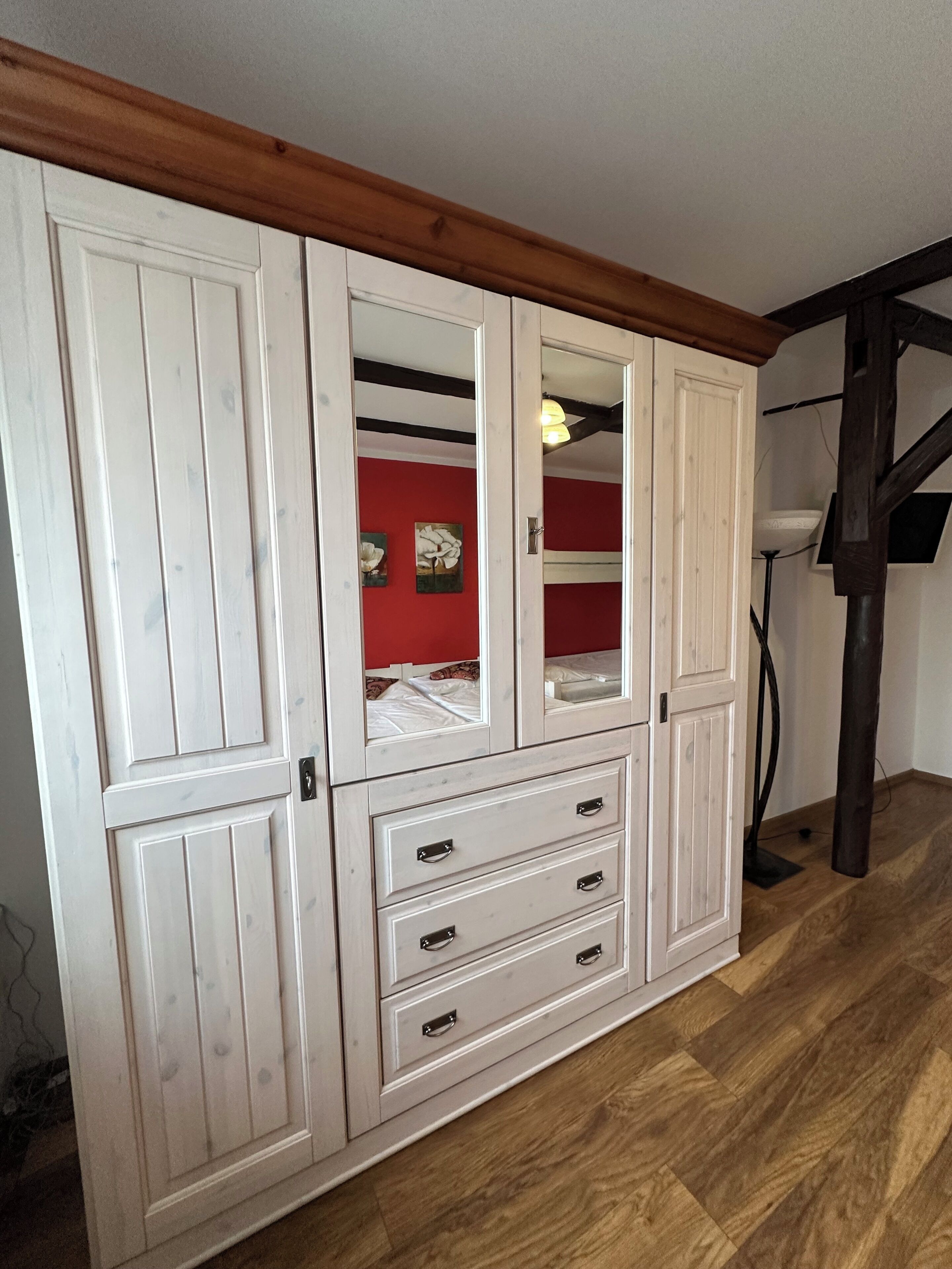 Un armario blanco de madera con varias puertas y cajones, una pared roja y una viga de madera en el techo.
