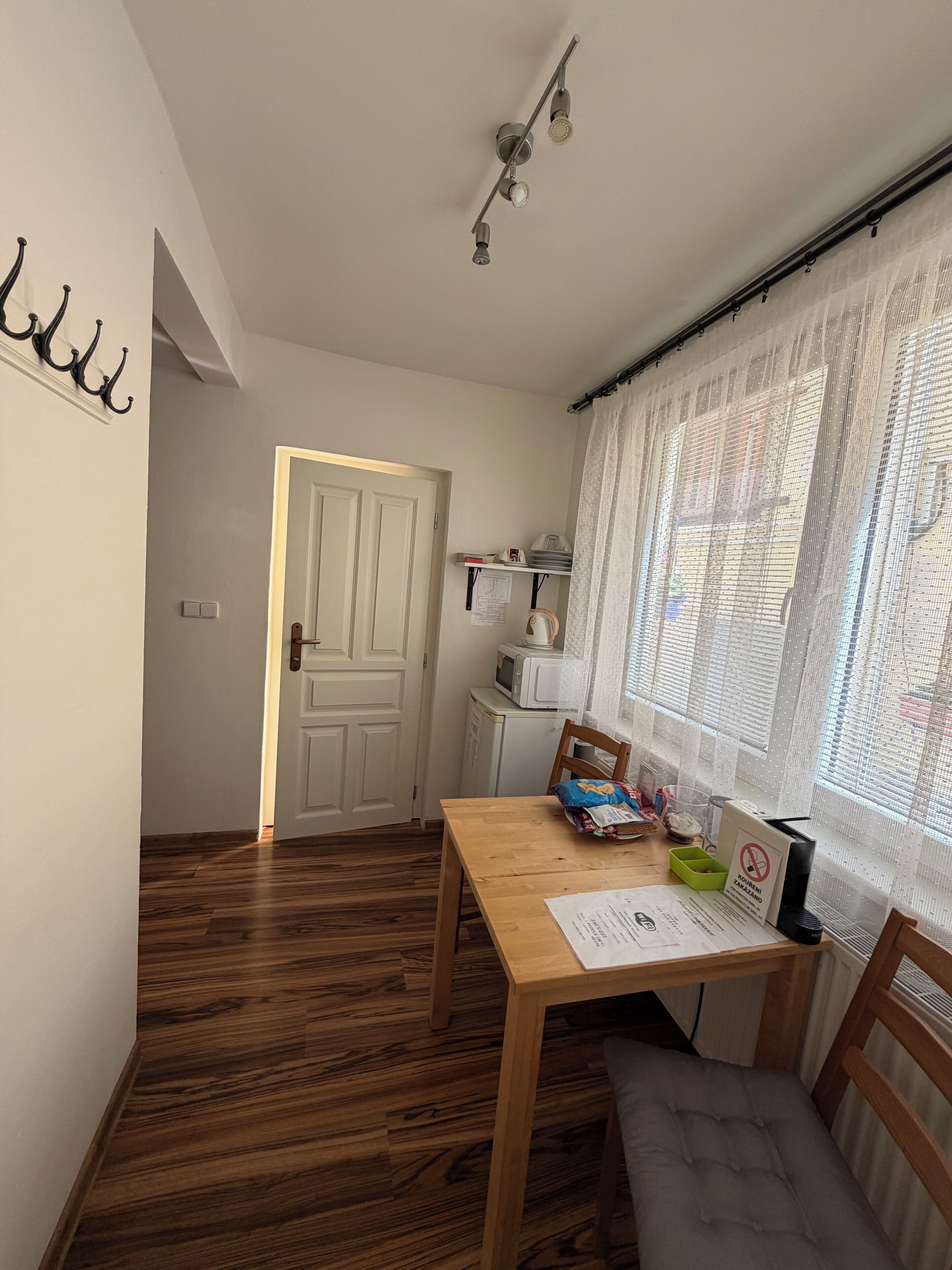 Una habitación con piso de madera, una mesa de comedor, una silla, microondas y una ventana con cortinas translúcidas.