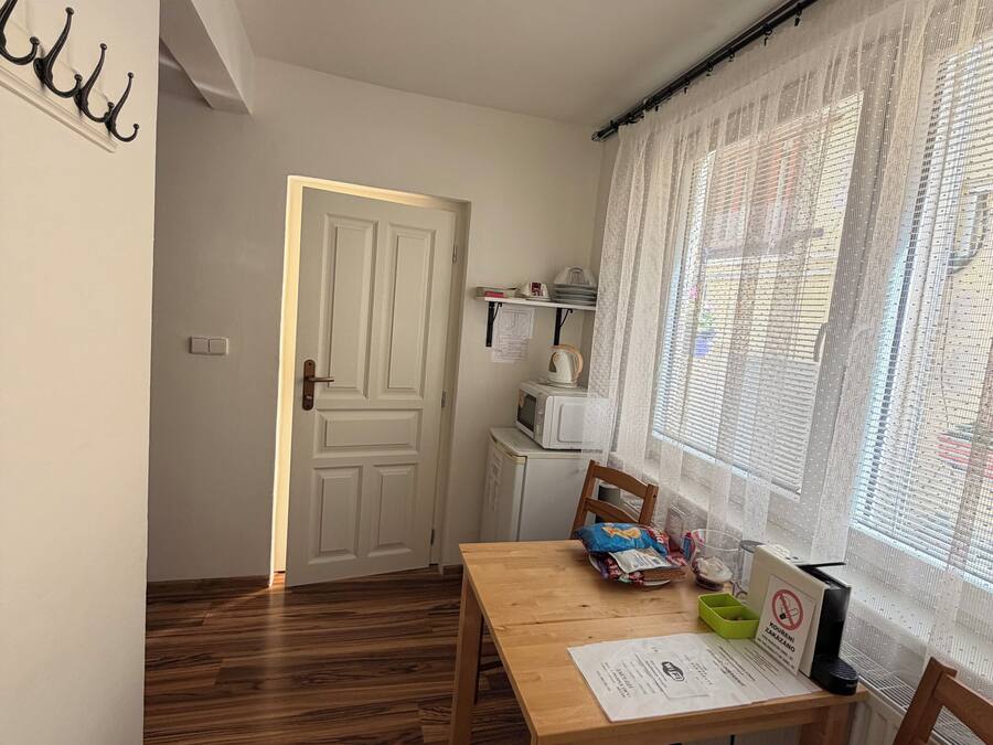 Una habitación con piso de madera, una mesa de comedor, una silla, microondas y una ventana con cortinas translúcidas.