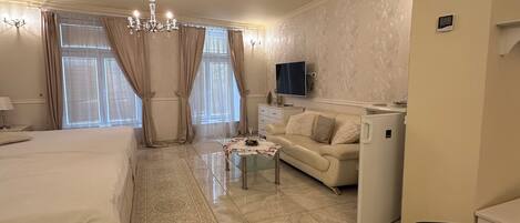A hotel room with a bed, a sofa, a TV, a minibar, and a trash bin.