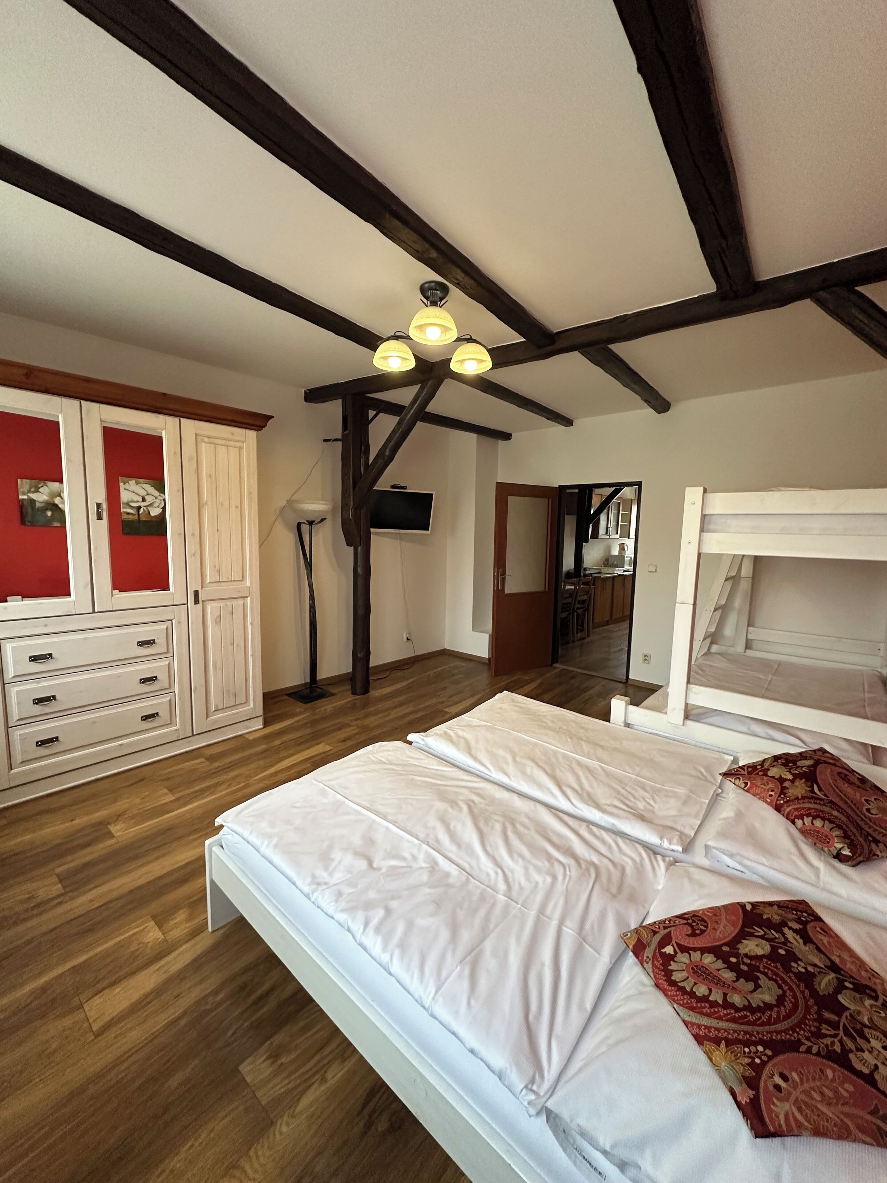 Een slaapkamer met houten vloer, een wit bed, een kledingkast en een plafondventilator.