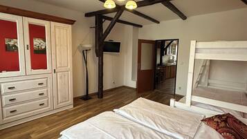 Een slaapkamer met houten vloer, een wit bed, een kledingkast en een plafondventilator.