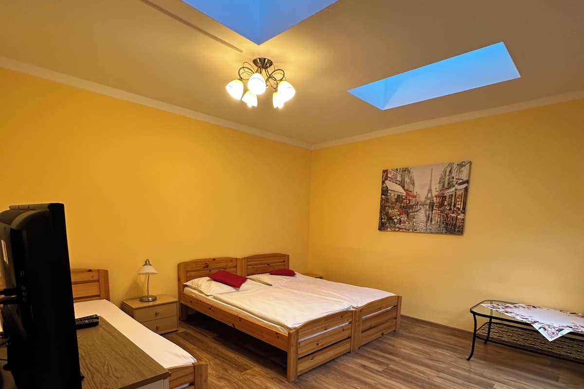 Une chambre avec une lucarne, un lit, un bureau, une chaise, une petite table et un tableau au mur.