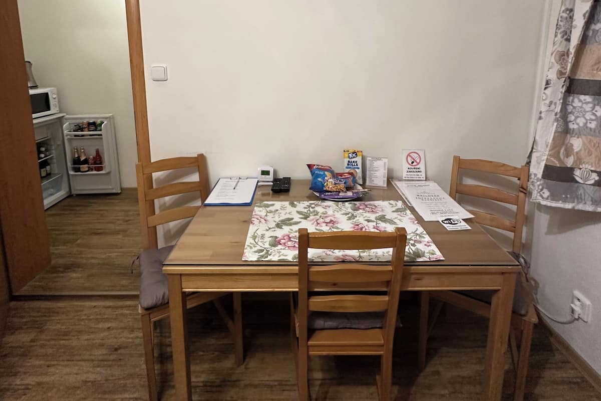 Un coin repas comprenant une table, des chaises, une nappe à motifs floraux, un climatiseur, un réfrigérateur et une porte donnant sur une autre pièce.