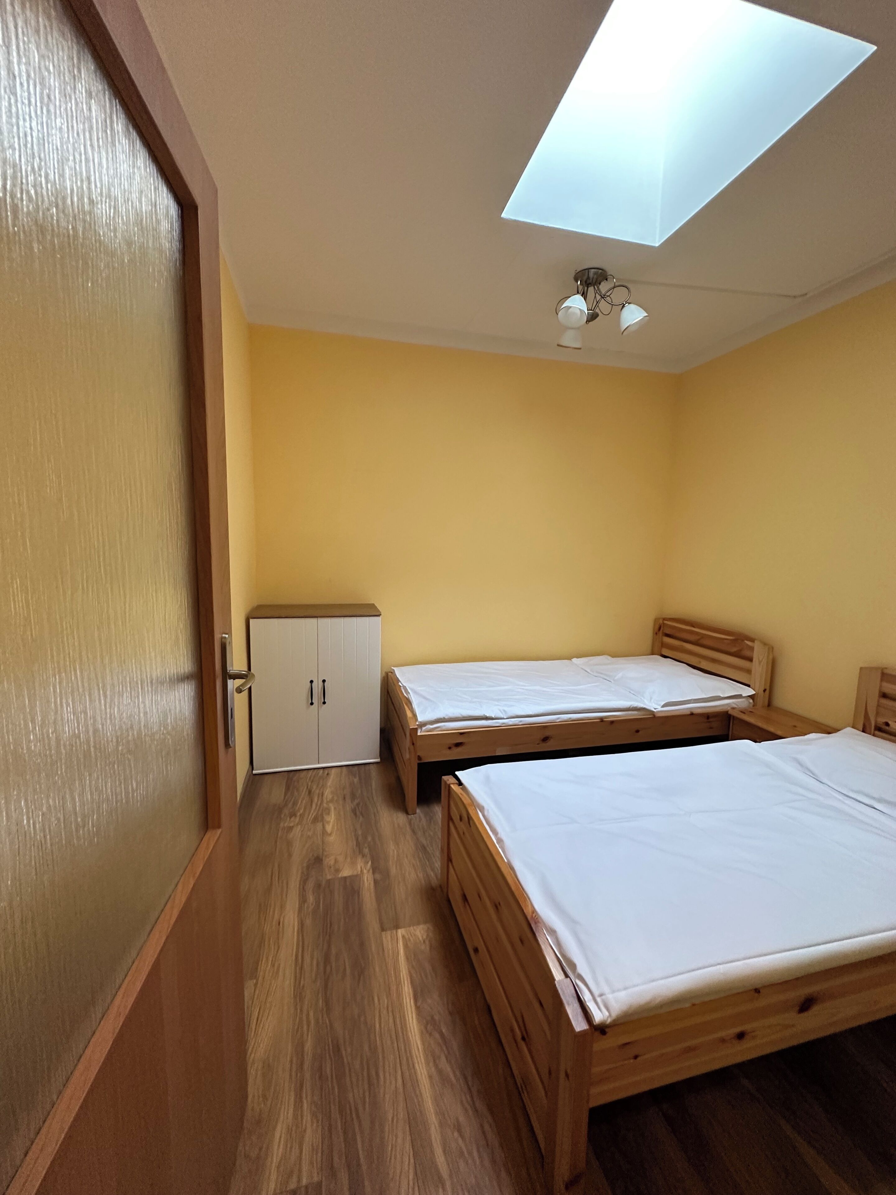 Una habitación con dos camas de madera, un armario y un tragaluz.