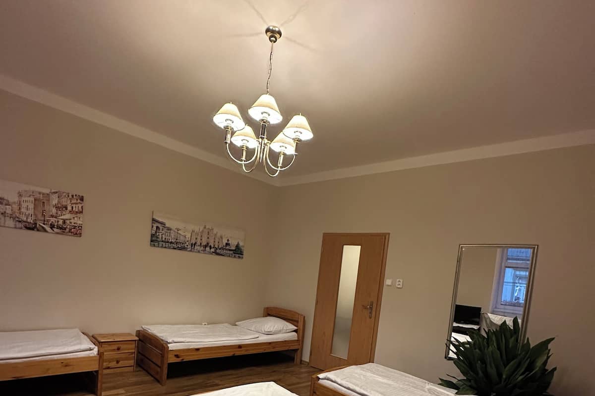 Une pièce avec quatre lits en bois, un plancher en bois, un lustre et un miroir au mur.