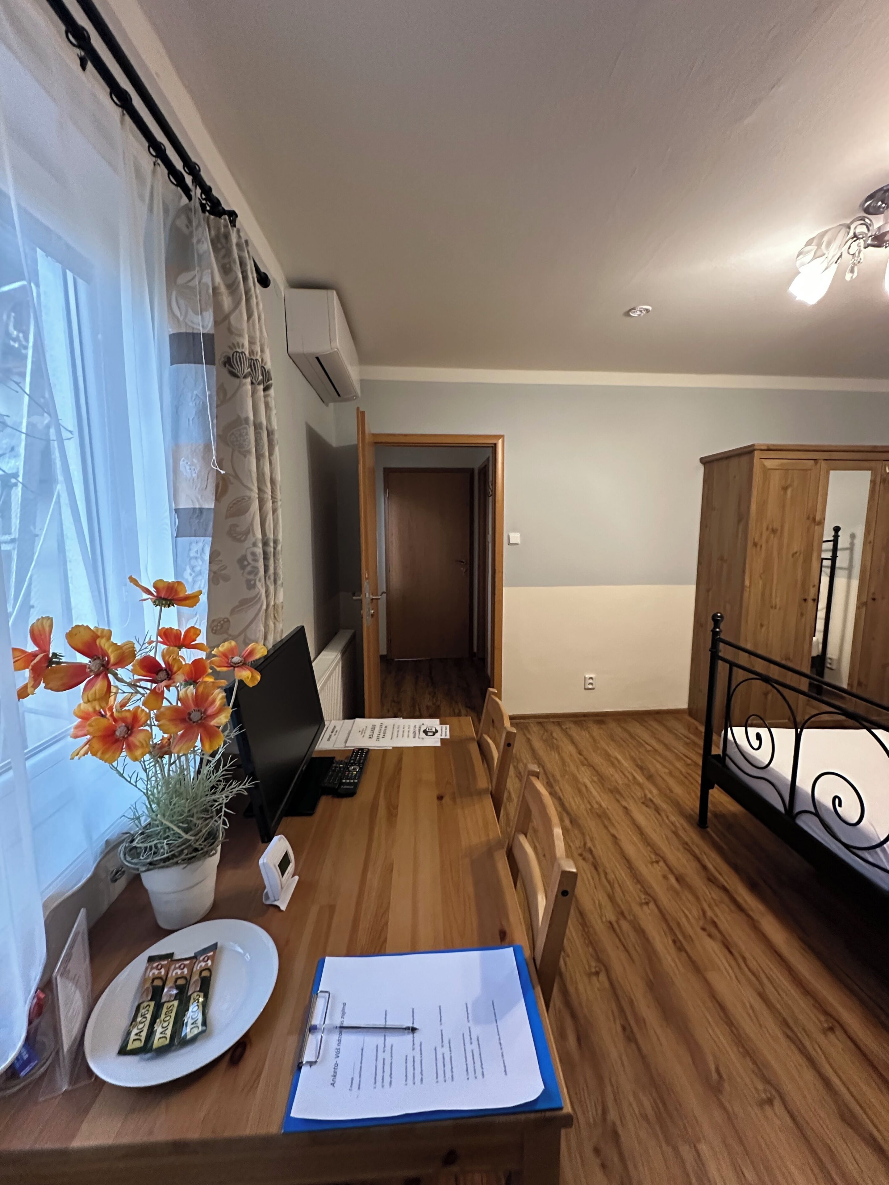 A room with a wooden dining table, a potted plant, a laptop, and papers on the table.