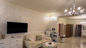 Una sala de estar con televisión de pantalla plana, un sofá, una mesa de centro, una araña y una zona de cocina.