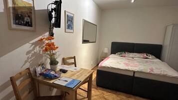 Una habitación pequeña y luminosa con una cama, un escritorio con silla y una planta en maceta.