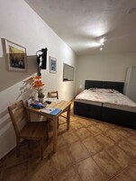 Una habitación pequeña y luminosa con una cama, un escritorio con silla y una planta en maceta.