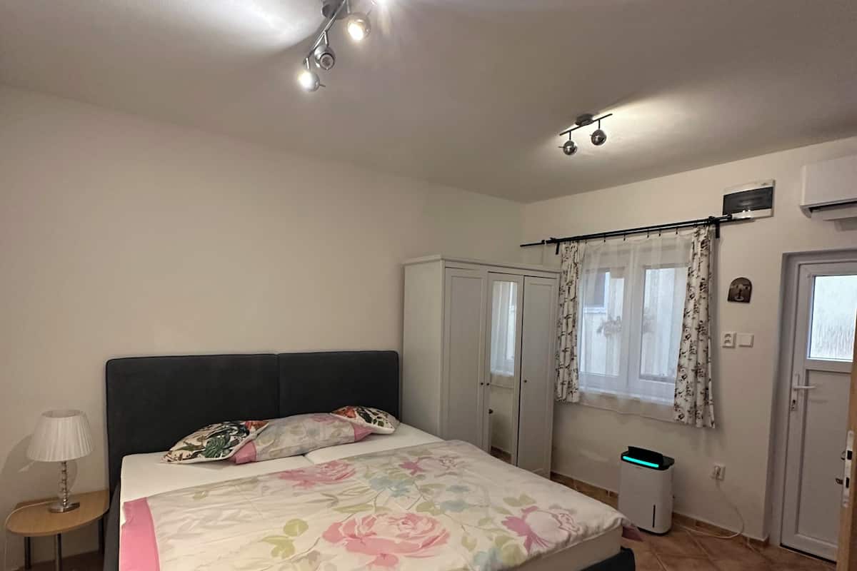 Une chambre à coucher comprenant un lit, une armoire, une table de chevet, une lampe, un appareil de climatisation et une fenêtre avec des rideaux.