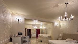 Habitación de hotel con cama, sofá, una pequeña mesa con mantel de flores, candelabro y baño al fondo.