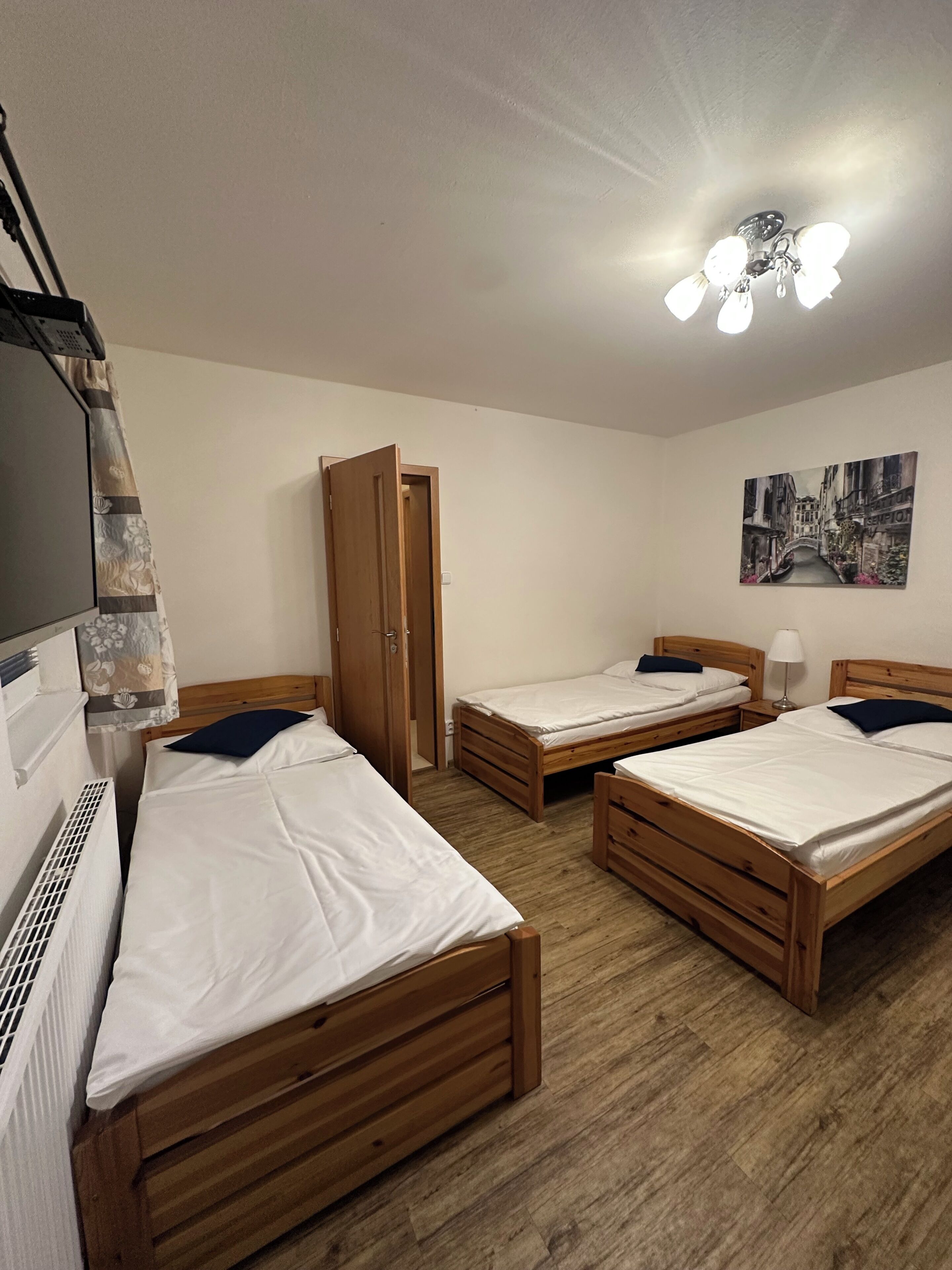 Quarto com quatro camas de madeira, um ventilador de teto, uma TV fixada na parede e um quadro de uma paisagem urbana.