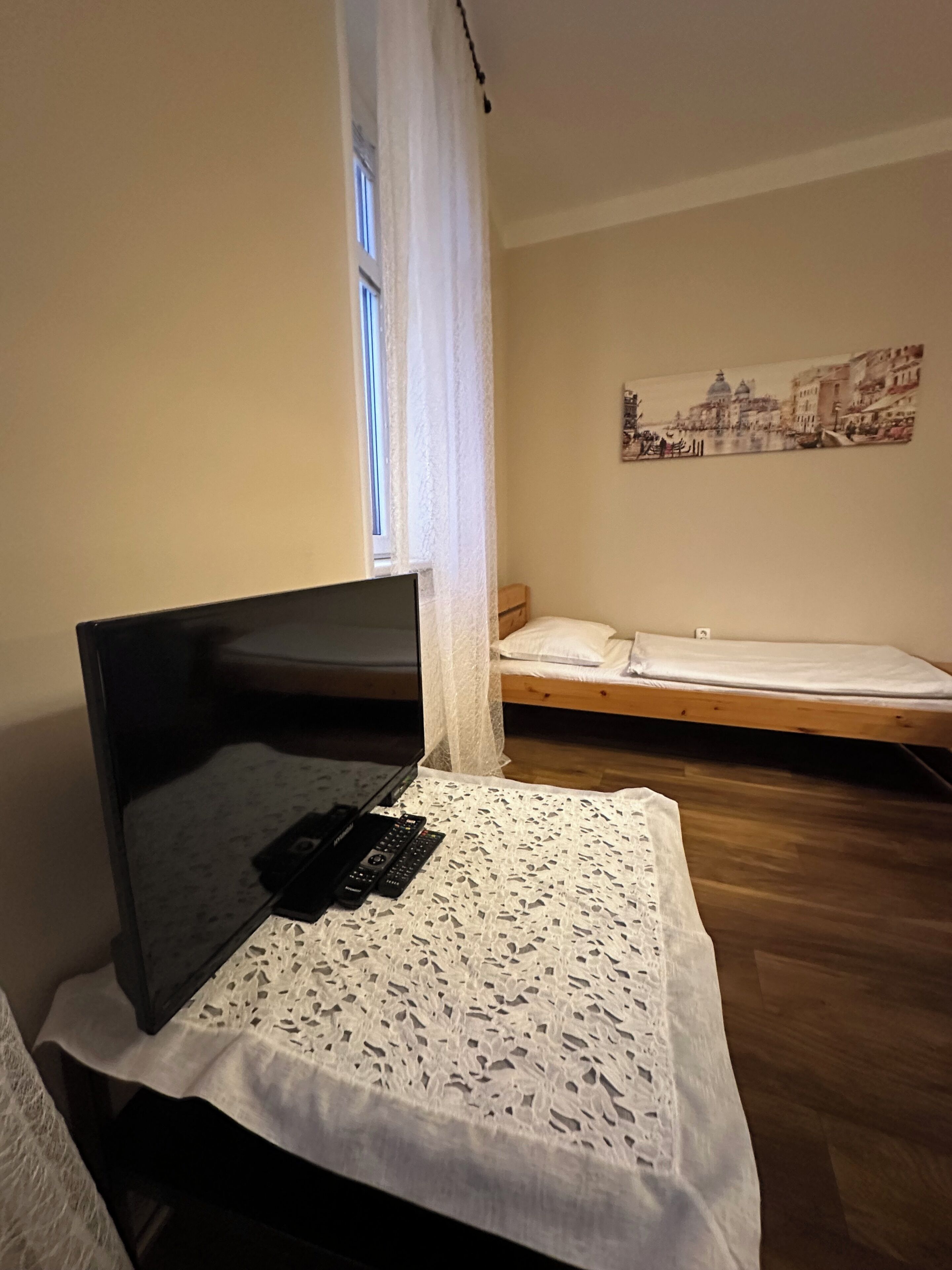 A room with a bed, a TV, and a table with remote controls.