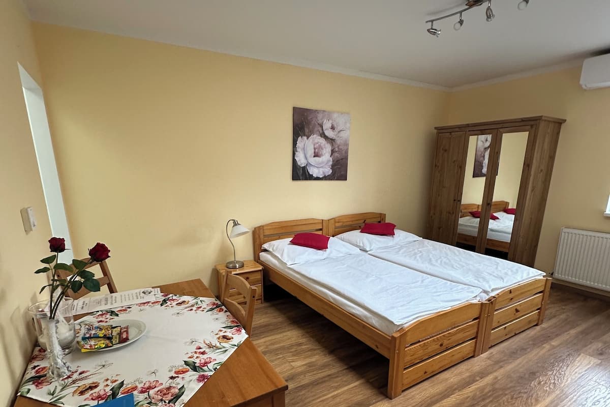 Une chambre à coucher avec un lit en bois, un bureau avec une chaise, un vase de fleurs et une lucarne.
