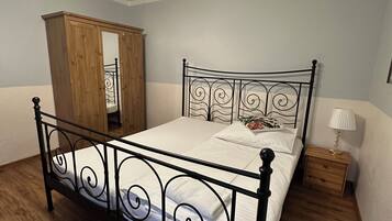 A bedroom with a metal-framed bed, wooden wardrobe, and a ceiling fan.