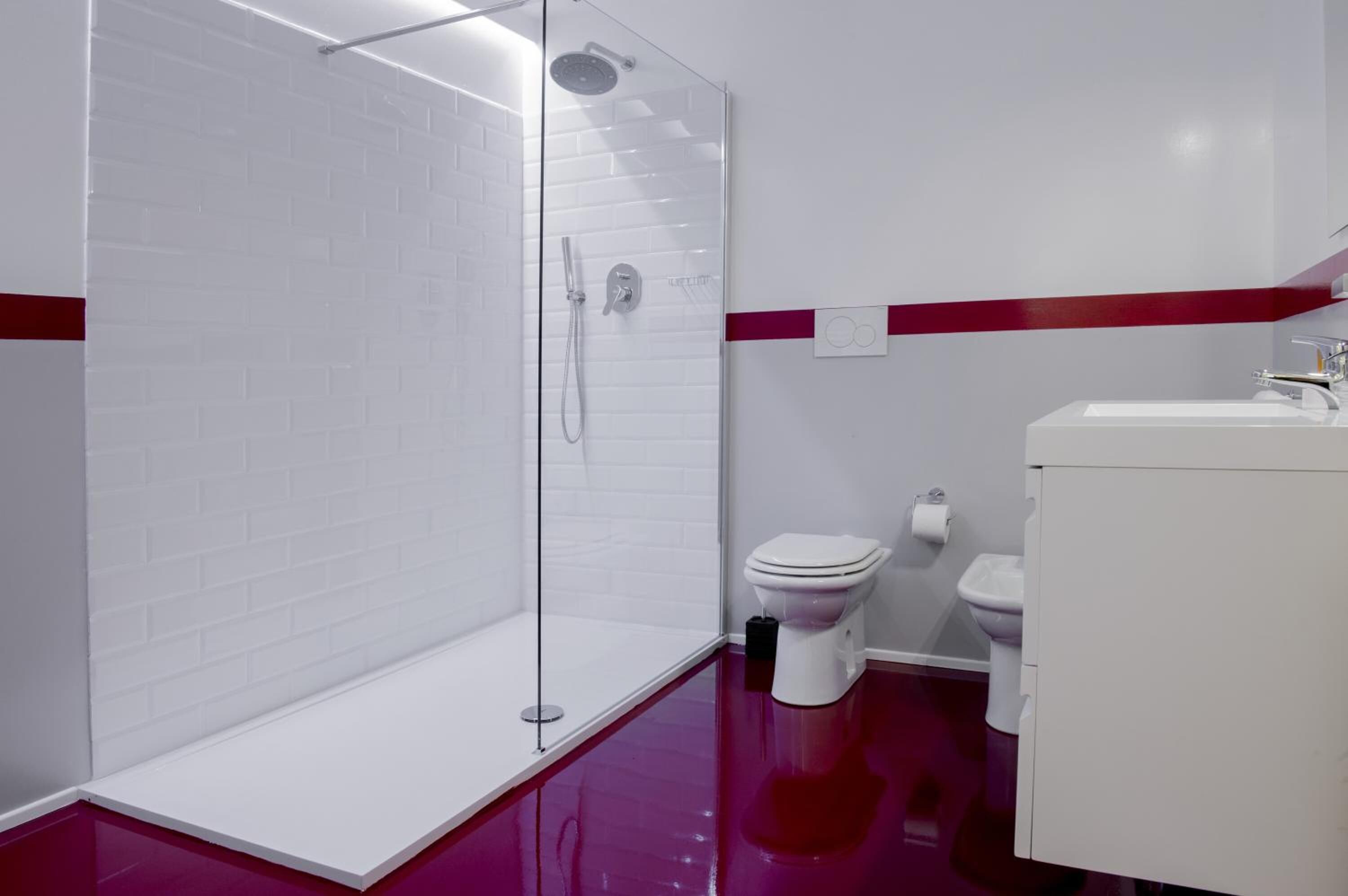 A modern bathroom with a glass-enclosed shower, white tiled walls, a red stripe, a white sink, and a toilet.