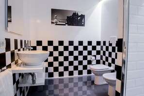A bathroom with a white sink, a toilet, and a checkered black and white tile wall. - B&B il Castelluccio (Arezzo)