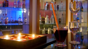 Una zona de bar con una bandeja de velas, un vaso de bebida roja con pajita y una copa de vino.