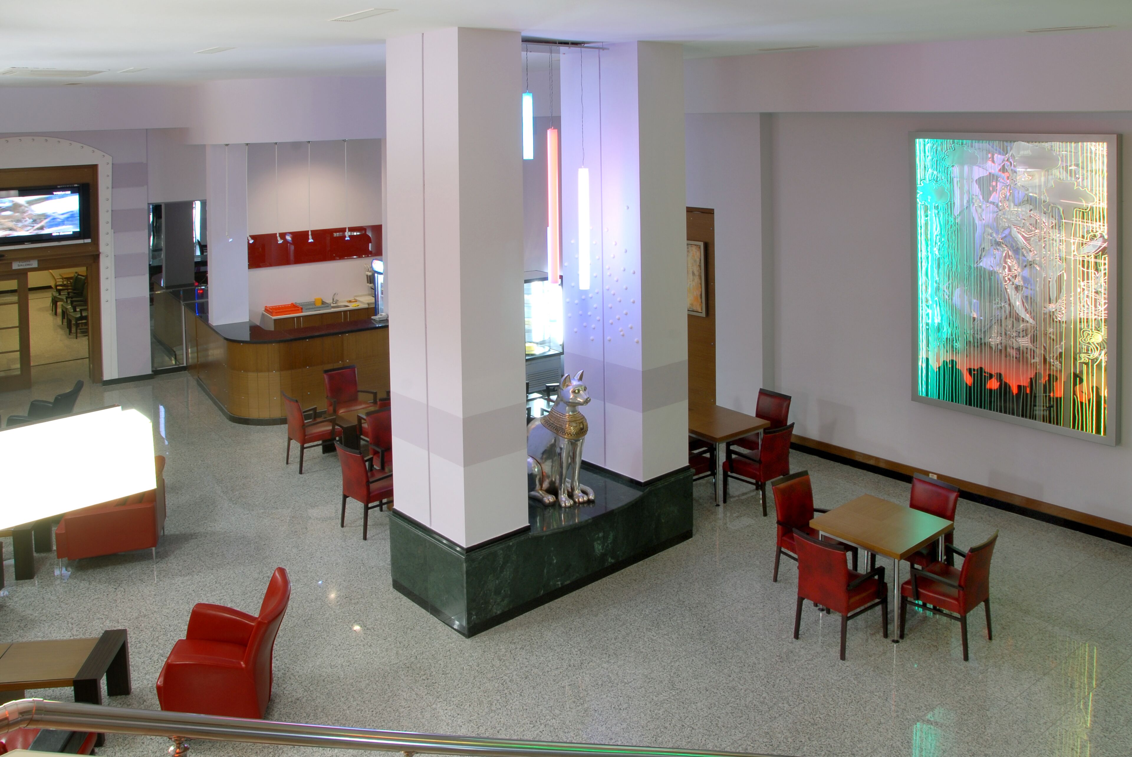 A modern lobby with a central seating area, a reception desk, and a large abstract art piece on the wall.