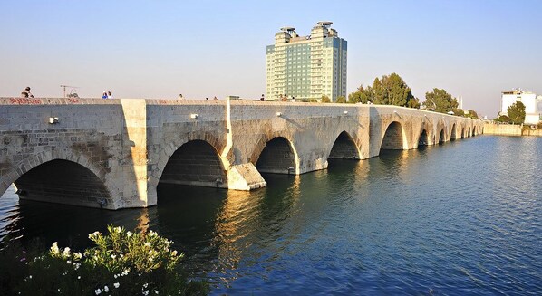 A stone bridge over a river with multiple arches, a modern building in the background, and a clear sky.