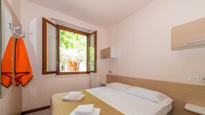 Un dormitorio con cama, ventana, toallero y mesita de noche.