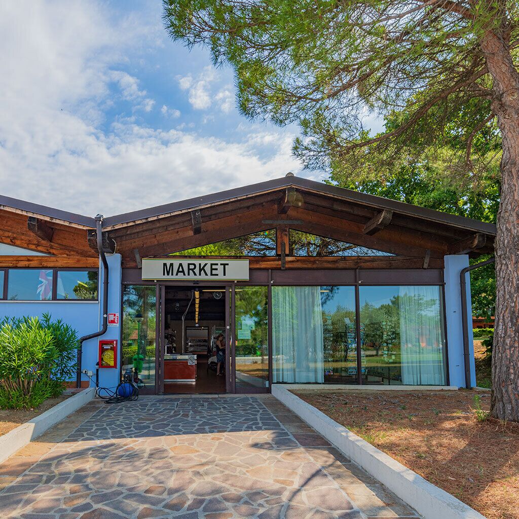 Un mercado con un letrero, estructura de madera, sendero de piedra y puertas de vidrio.
