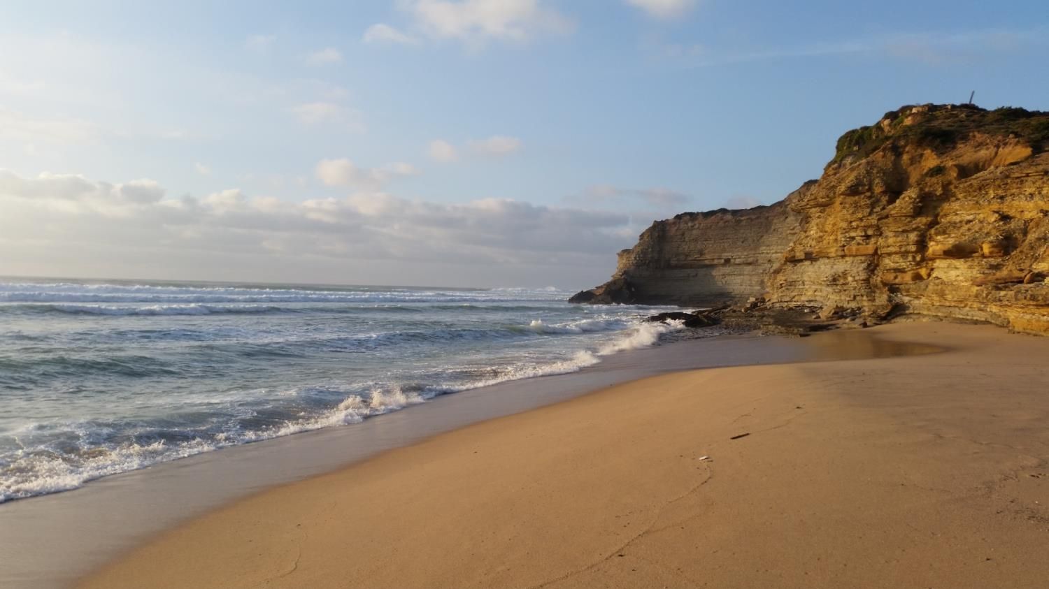 A beach with a sandy shore and a rocky cliff.