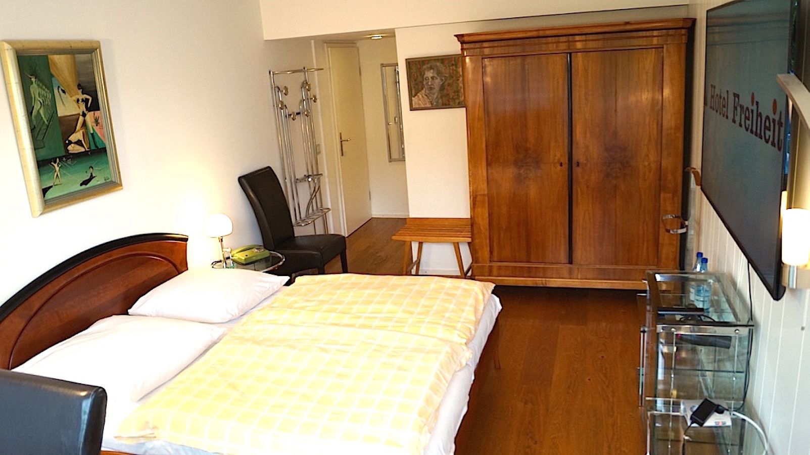A hotel room with a bed, a chair, a desk, a wardrobe, and a television.