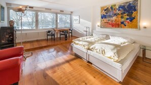 A bedroom with a large bed, a desk, and a chair. There is a window with a view of trees and a radiator under the window. - Hotel Freiheit (Cologne)