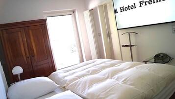 A hotel room with a bed, a wooden wardrobe, a window with curtains, and a sign on the wall.