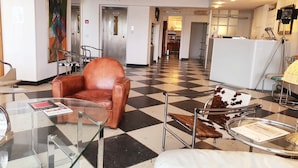 A lobby with a checkered floor, a brown leather armchair, a glass table, and a white sofa. - Hotel Freiheit (Cologne)
