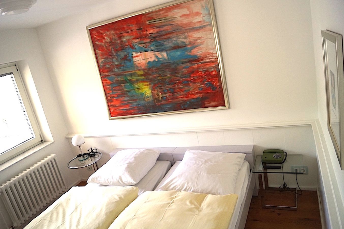 Ein Schlafzimmer mit Bett, Fenster, Heizkörper, Nachttisch, Lampe und Telefon.